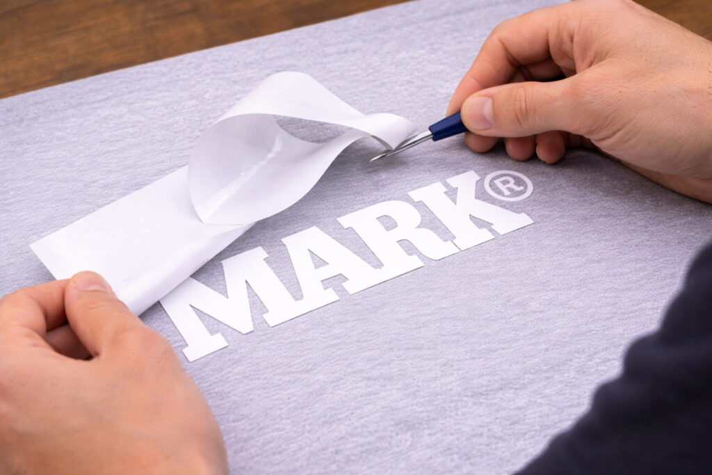 Proceso de weeding de vinil textil retirando excedente sobre playera con logo de Mark